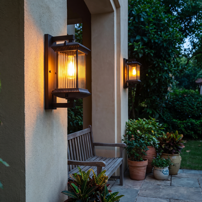 Wall lantern glowing on a covered porch at blue hour with plants and a bench