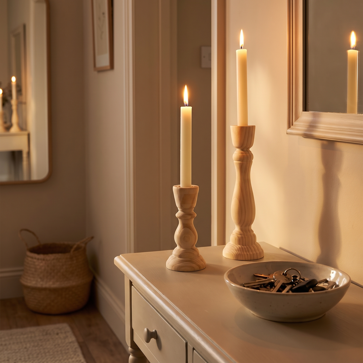 A short and a tall turned wooden candlestick lit on a hallway console