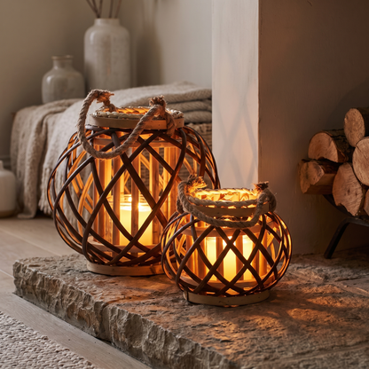 A large and a small woven wicker lantern lit on a stone hearth