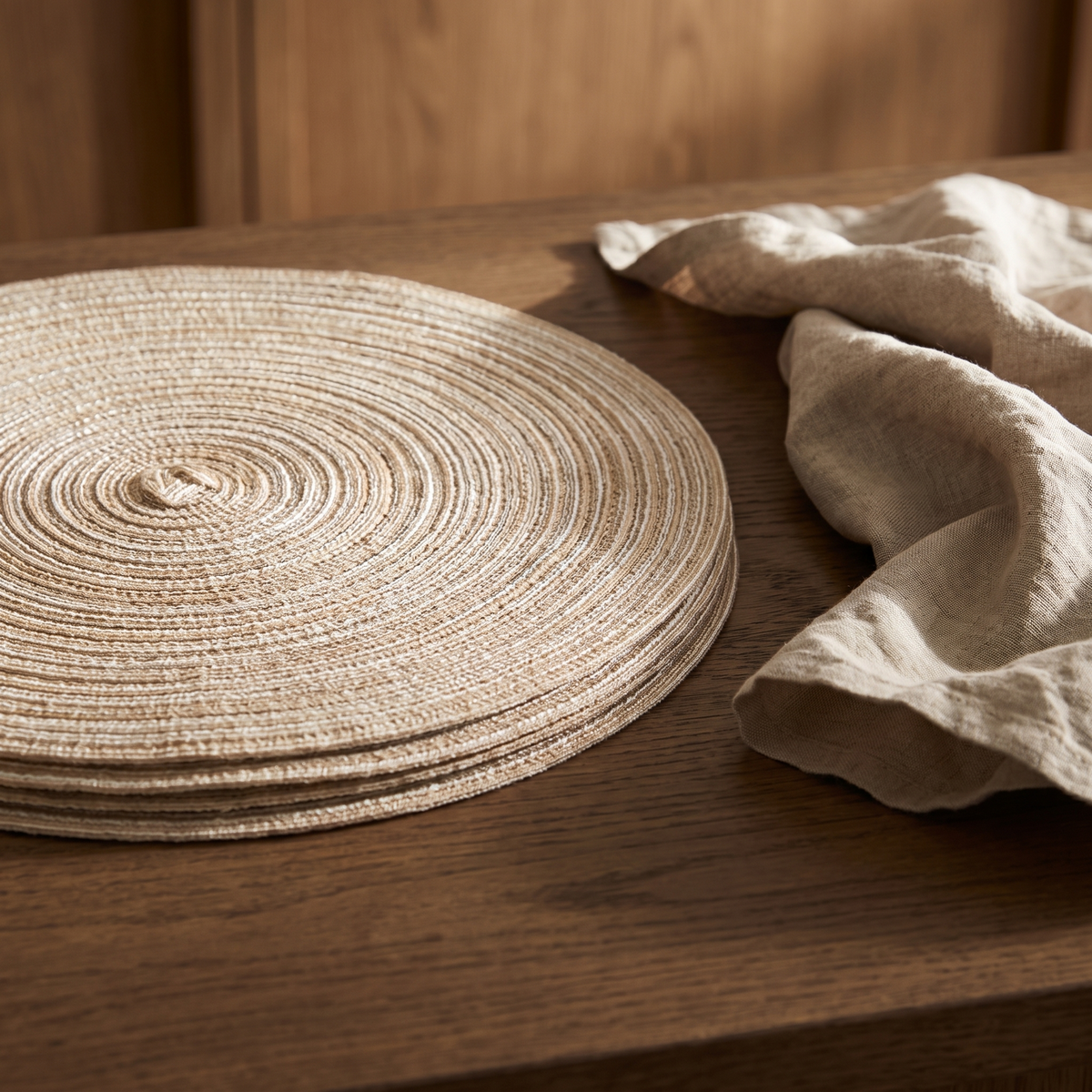 A stack of braided cotton cord placemats on a dark worktop